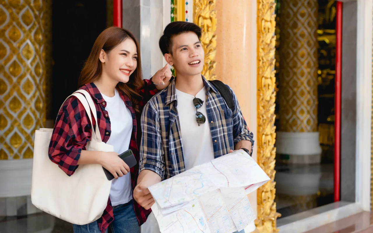 smiley-asian-couple-tourist-backpackers-standing-beautiful-thai-temple-pretty-woman-holding-paper-map-handsome-man-check-smartphone-with-happy-vacations